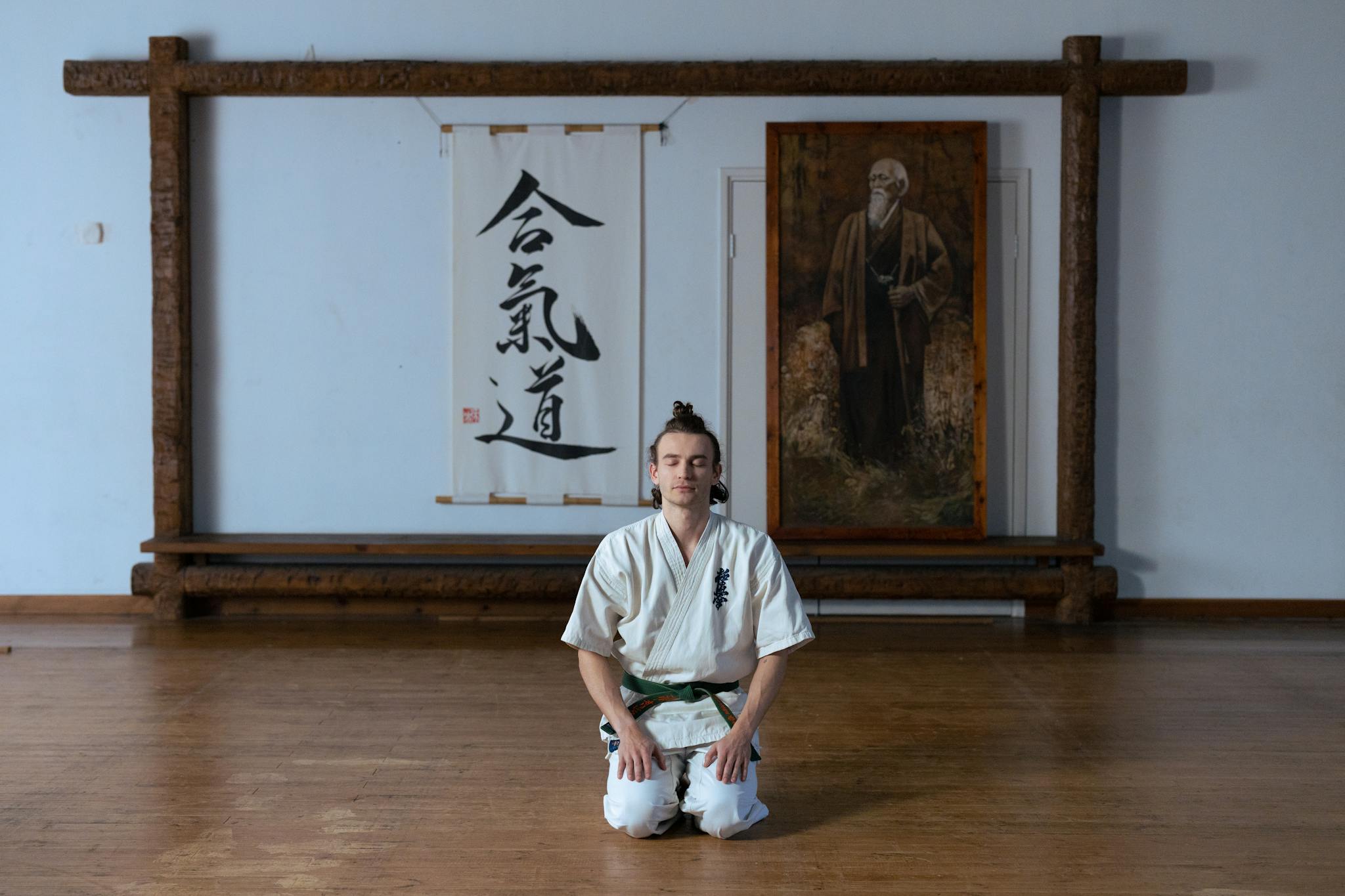 A man in traditional martial arts attire meditates peacefully in a dojo, emphasizing mindfulness.