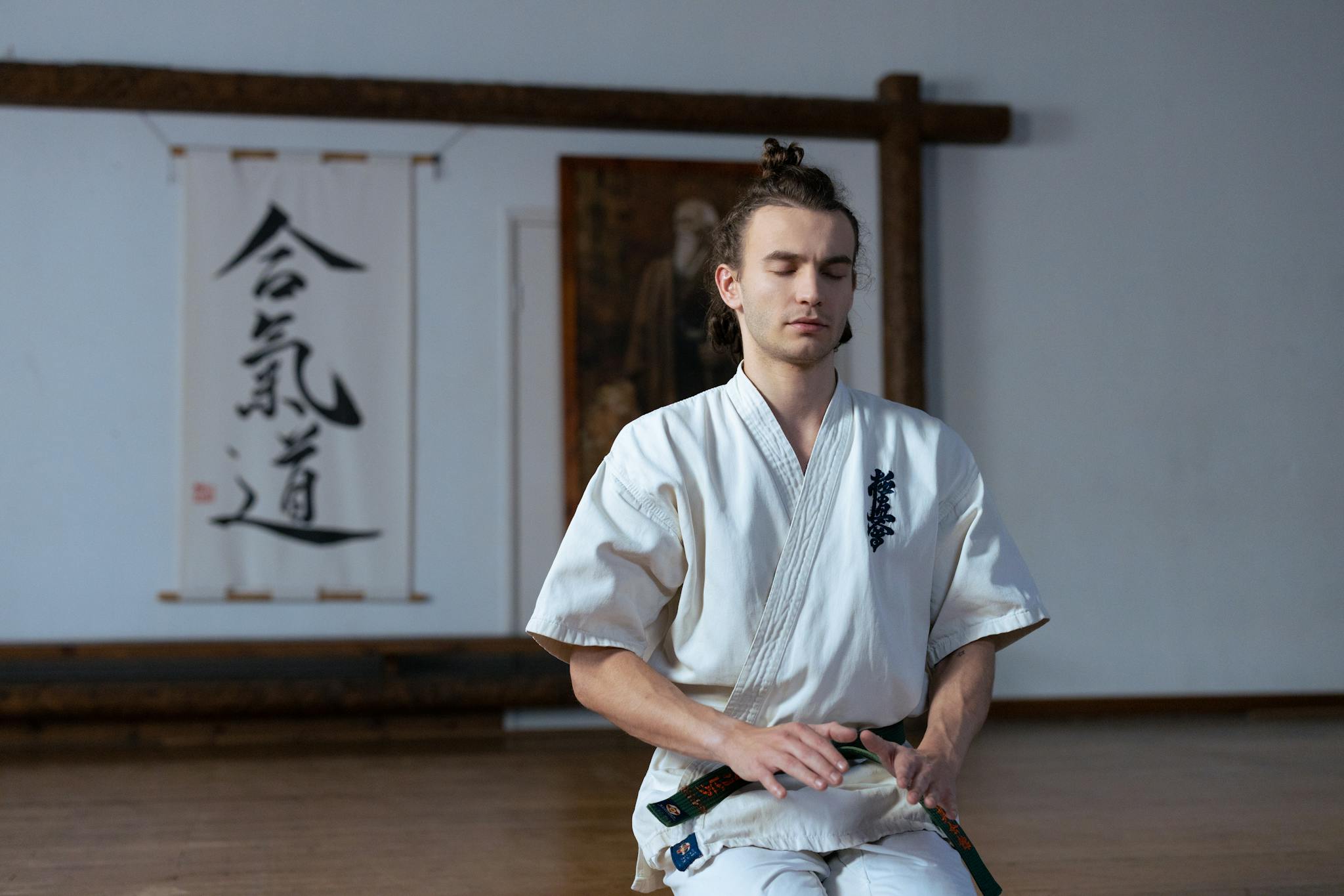 Man in martial arts uniform meditating in a dojo with peaceful expression, focusing on mindfulness.