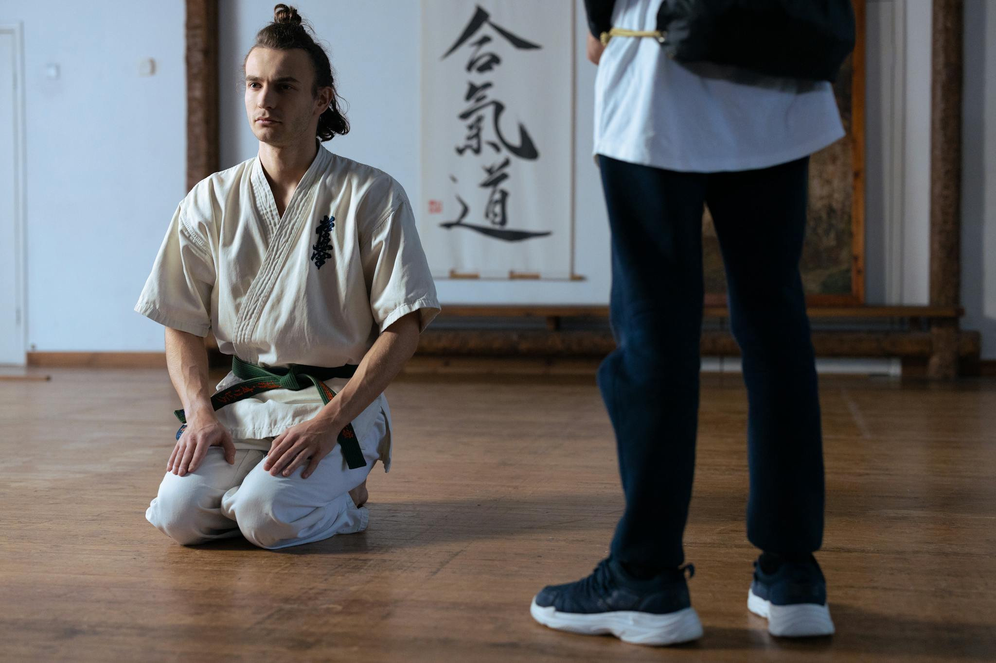 Martial artist in traditional training attire kneeling in a dojo, focused and poised.
