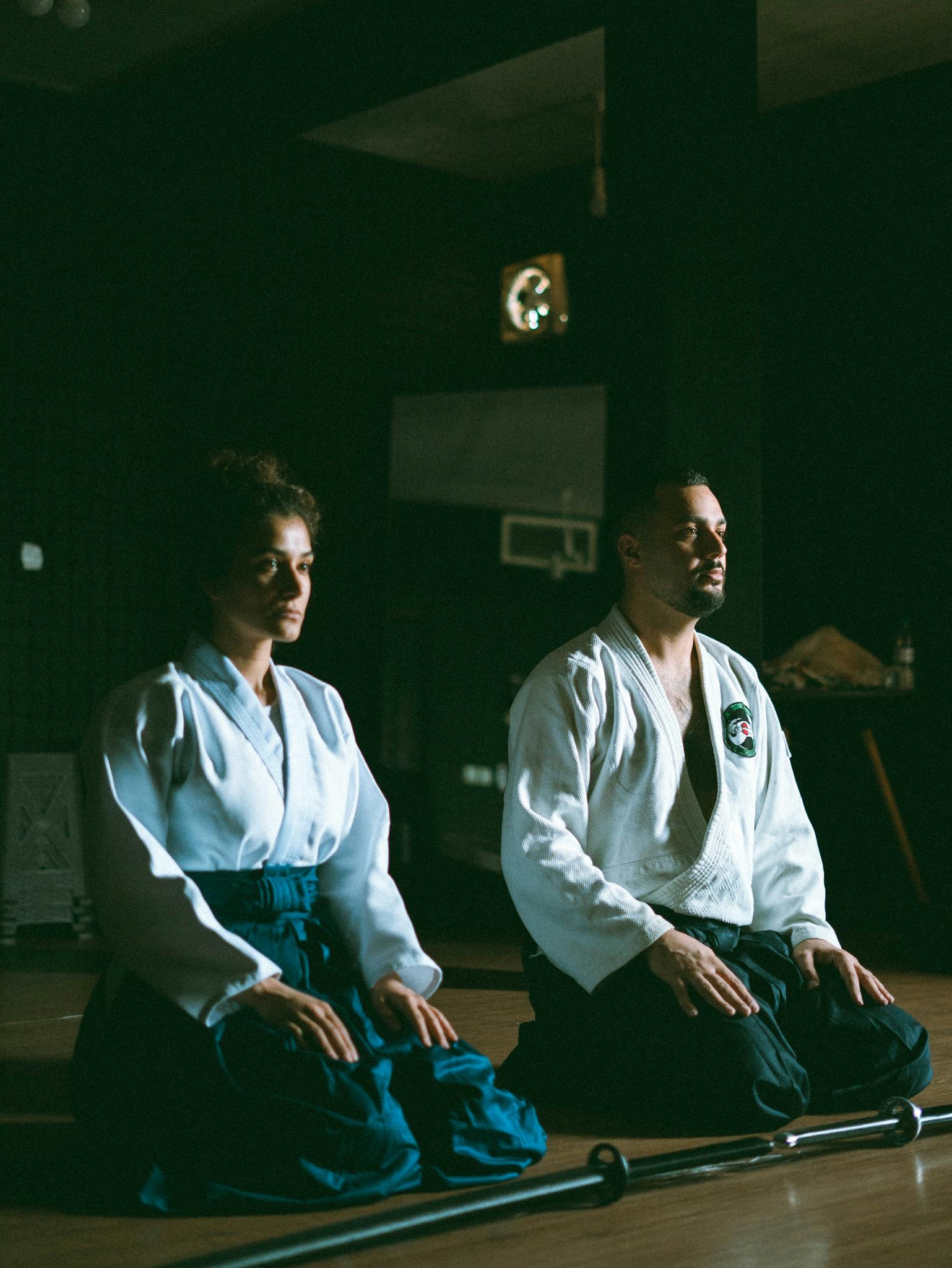 Martial artists in traditional attire practicing meditation indoors.