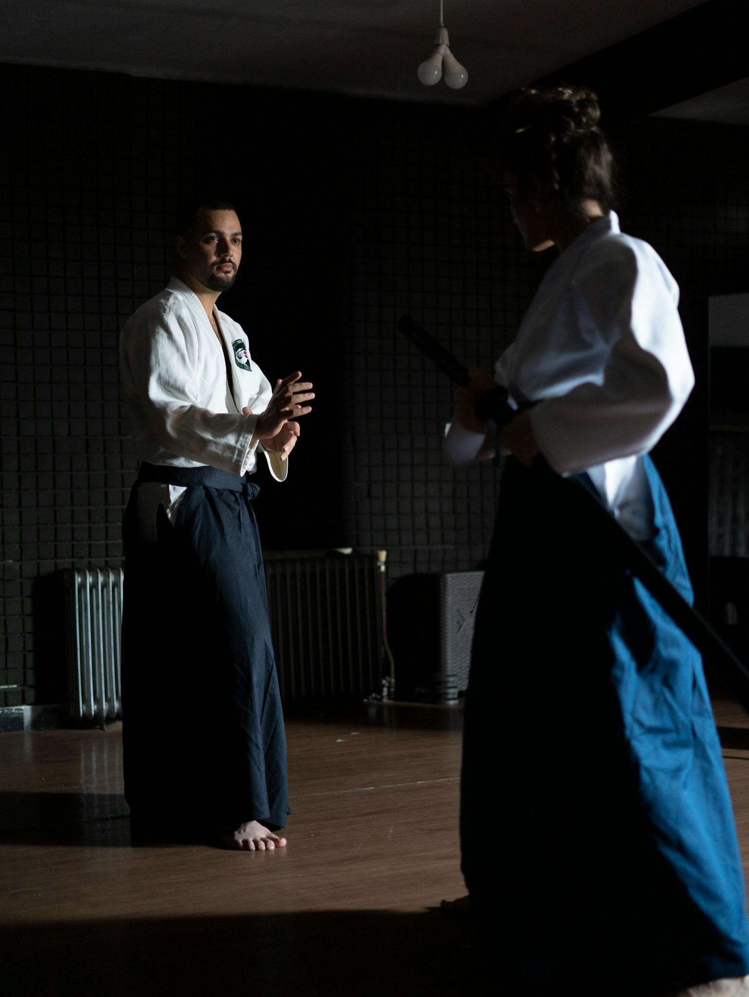 Two adults practicing martial arts in a dimly lit dojo, focused and poised.
