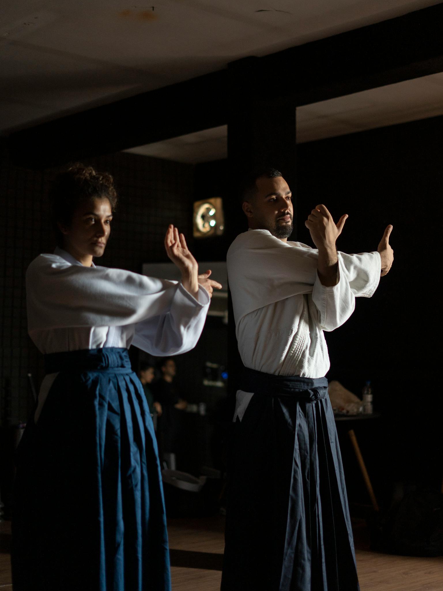 Two adults practicing martial arts indoors wearing traditional clothing.